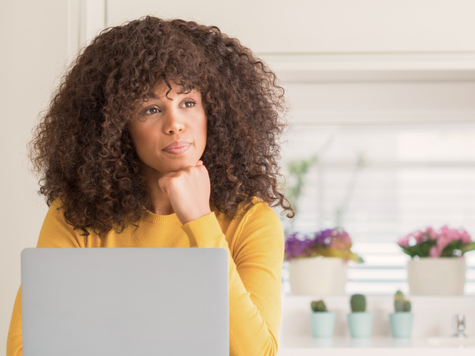 Une femme réfléchit face à son ordinateur portable.