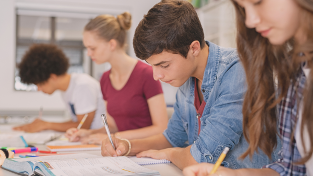 Des collégiens prennent des notes dans leur cahier.