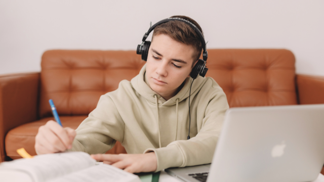 Un collégien fait ses devoirs sur son ordinateur et son manuel.