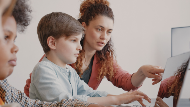 Une professeure conseille une élève de primaire sur l'ordinateur.