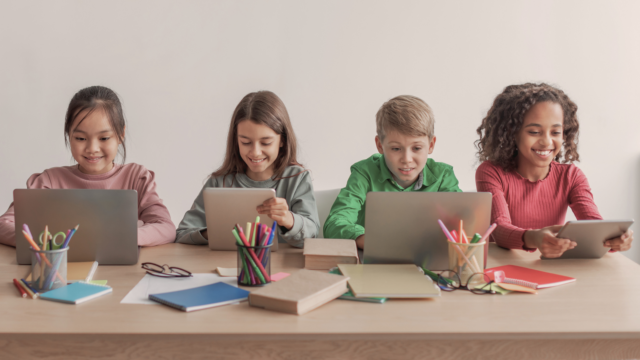 Quatre élèves de primaire étudient sur des tablettes et des ordinateurs.