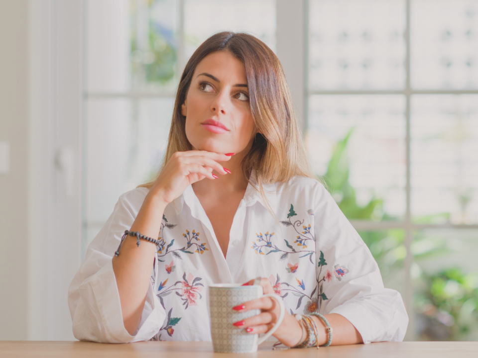 Une femme réfléchit avec une tasse à la main.