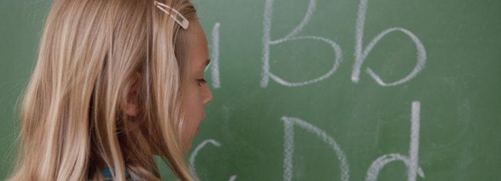 Une élève écrit des lettres sur un tableau à craie.