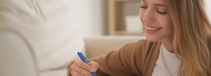 Une femme écrit une lettre en souriant.