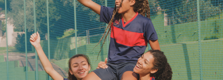 Trois jeunes filles célèbrent leur victoire au foot, l'une est portée sur les épaules des deux autres.