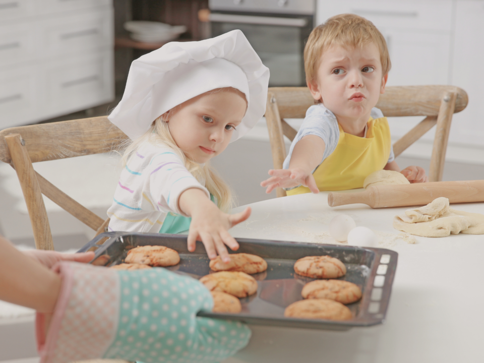 Des enfants tendent les bras pour manger des biscuits tout juste sortis du four.