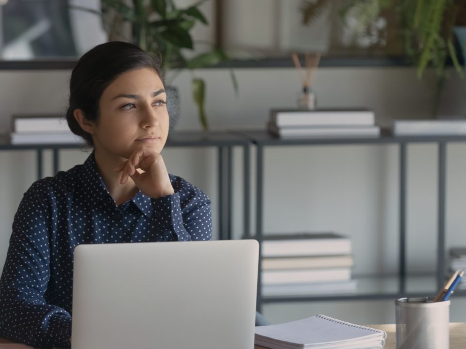 Une femme réfléchit devant son ordinateur portable.