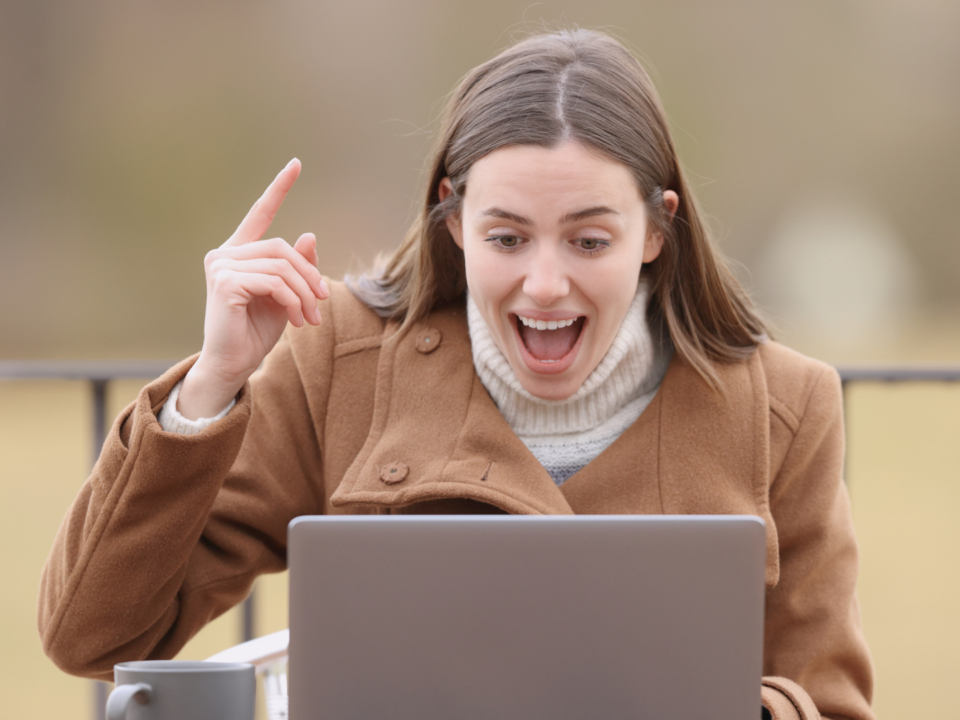 Une femme est surprise, index en l'air devant son ordinateur.