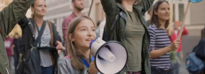 Une foule manifeste, une enfant parle dans un mégaphone.