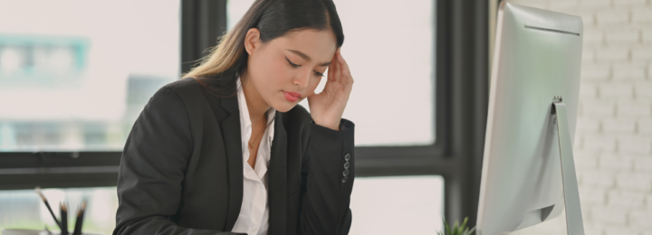 Une femme, visiblement préoccupée, se tient la tête en lisant le contenu affiché sur sa tablette, posée sur son bureau.