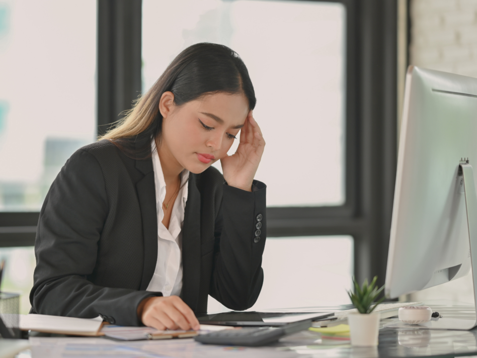 Une femme, visiblement préoccupée, se tient la tête en lisant le contenu affiché sur sa tablette, posée sur son bureau.