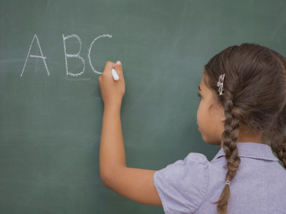 Une petite fille écrit sur un tableau à la craie.