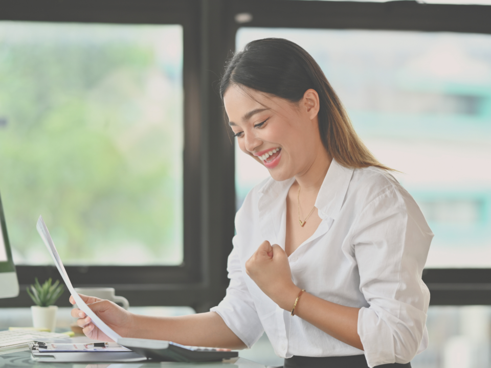 Une femme assise à son bureau est joyeuse en regardant un papier.