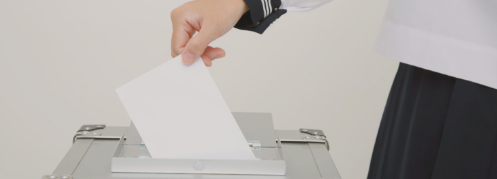 Une main féminine dépose son bulletin de vote dans une urne.