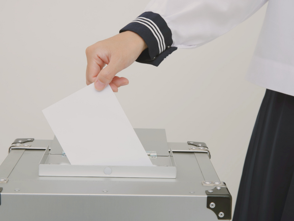 Une main féminine dépose son bulletin de vote dans une urne.