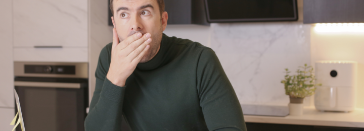 Un homme en télétravail dans sa cuisine semble surpris, la main sur la bouche.