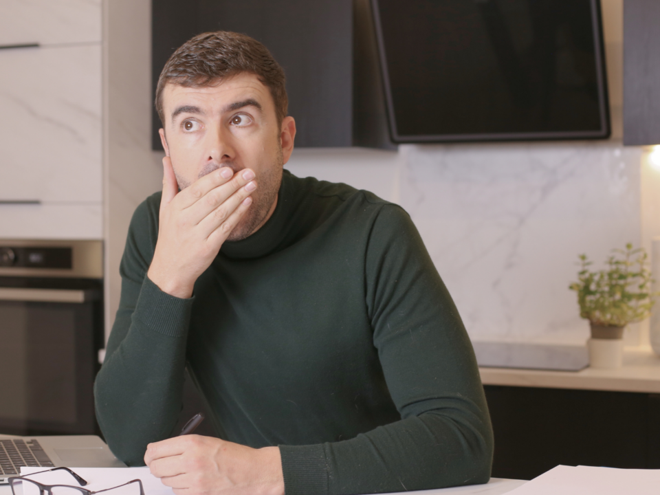 Un homme en télétravail dans sa cuisine semble surpris, la main sur la bouche.
