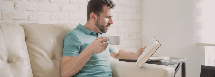 Un homme boit une tasse café en lisant un roman.