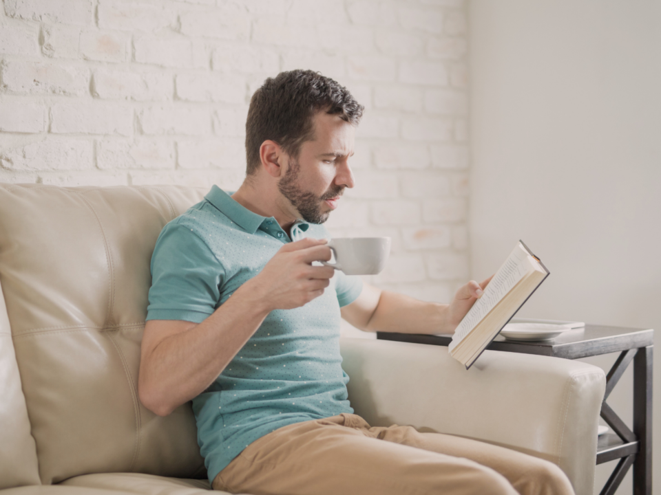 Un homme boit une tasse café en lisant un roman.