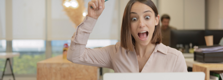 Une femme surprise regarde son ordinateur portable, le doigt levé.