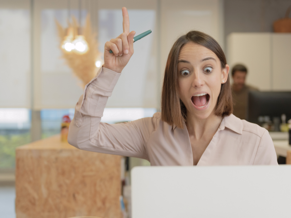 Une femme surprise regarde son ordinateur portable, le doigt levé.