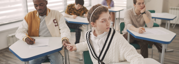 En classe, une élève passe discrètement un papier à un camarade assis derrière elle.