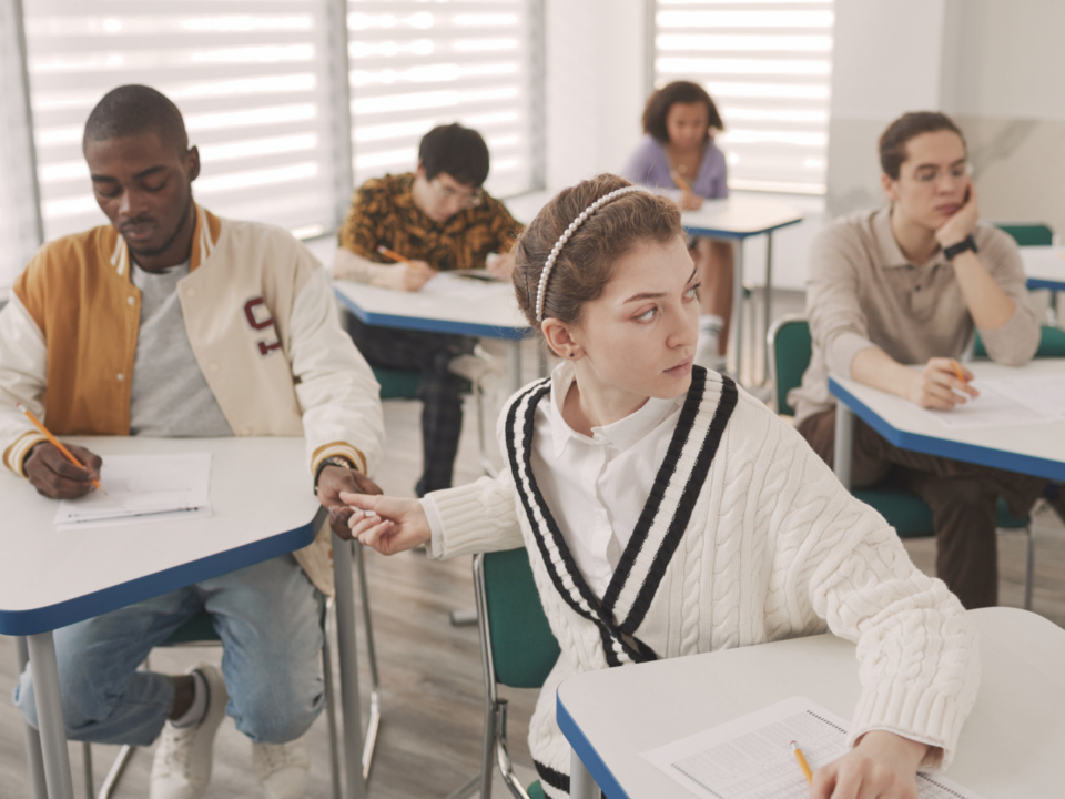 En classe, une élève passe discrètement un papier à un camarade assis derrière elle.