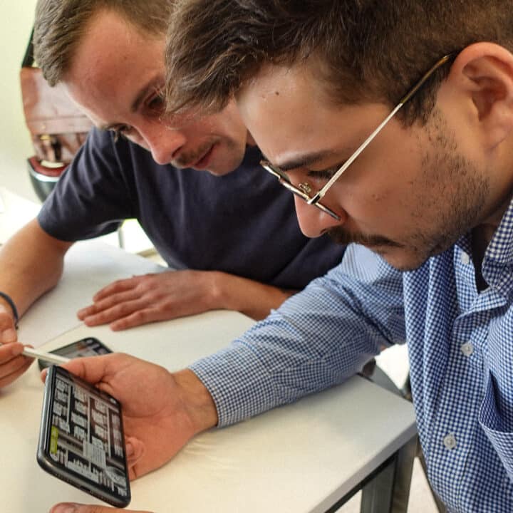 Deux hommes concentrés consultent l'application pédagogique Revolt-IA sur un smartphone.