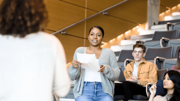 Une étudiante s’exprime à l’oral devant une classe en amphithéâtre.