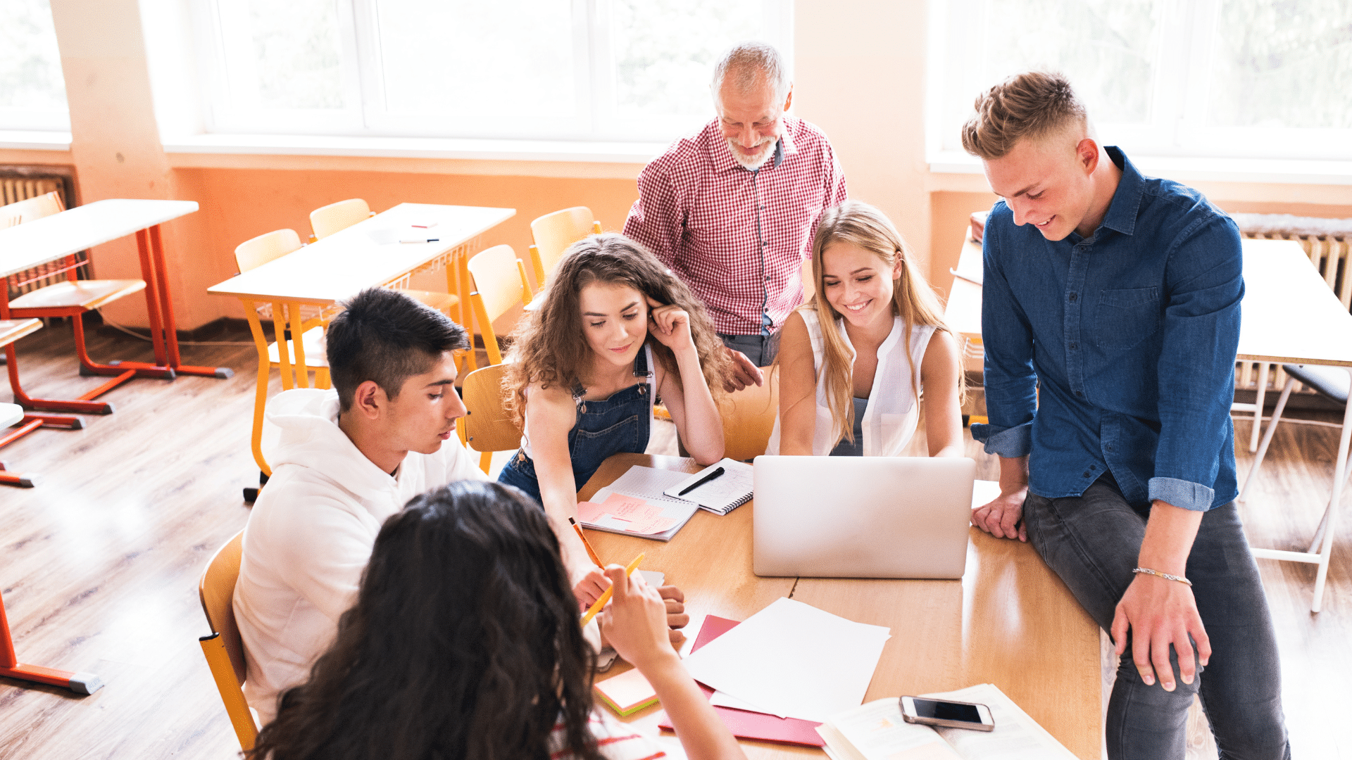 Un groupe de lycéens travaille en équipe autour d’un ordinateur portable, accompagné par un enseignant.